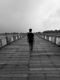 Rear view of man walking on pier against sky