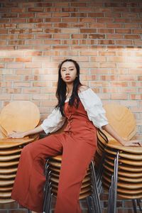 Young woman sitting against brick wall