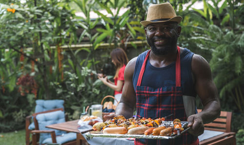 Portrait of smiling man holding tray with meat against woman 