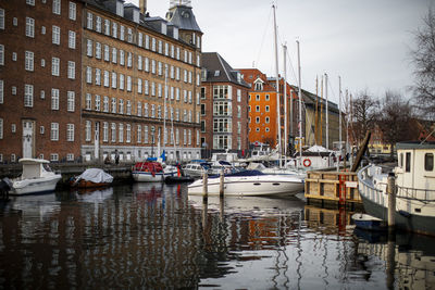 Sailboats moored on canal amidst buildings in city against sky