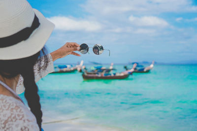 Woman holding sunglasses against sea at beach