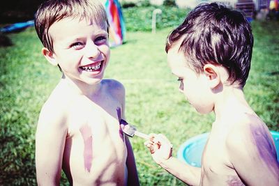 Side view of boy painting friends chest in yard