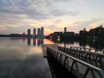 Scenic view of river by buildings against sky during sunset