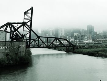 Bridge over river by buildings against sky in city