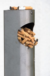 Close-up of cigarette butts in metallic garbage bin against white background