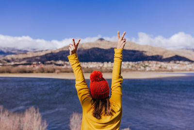 Rear view of woman with arms raised standing by sea against sky