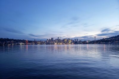 Illuminated city by sea against sky