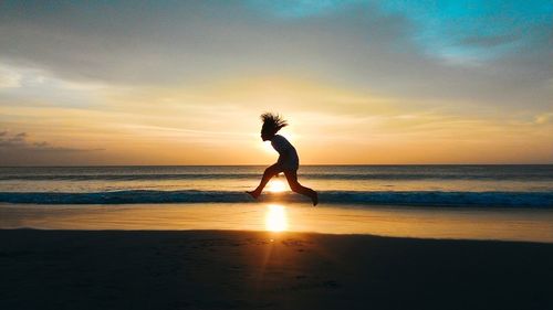 Silhouette woman on beach against sky during sunset