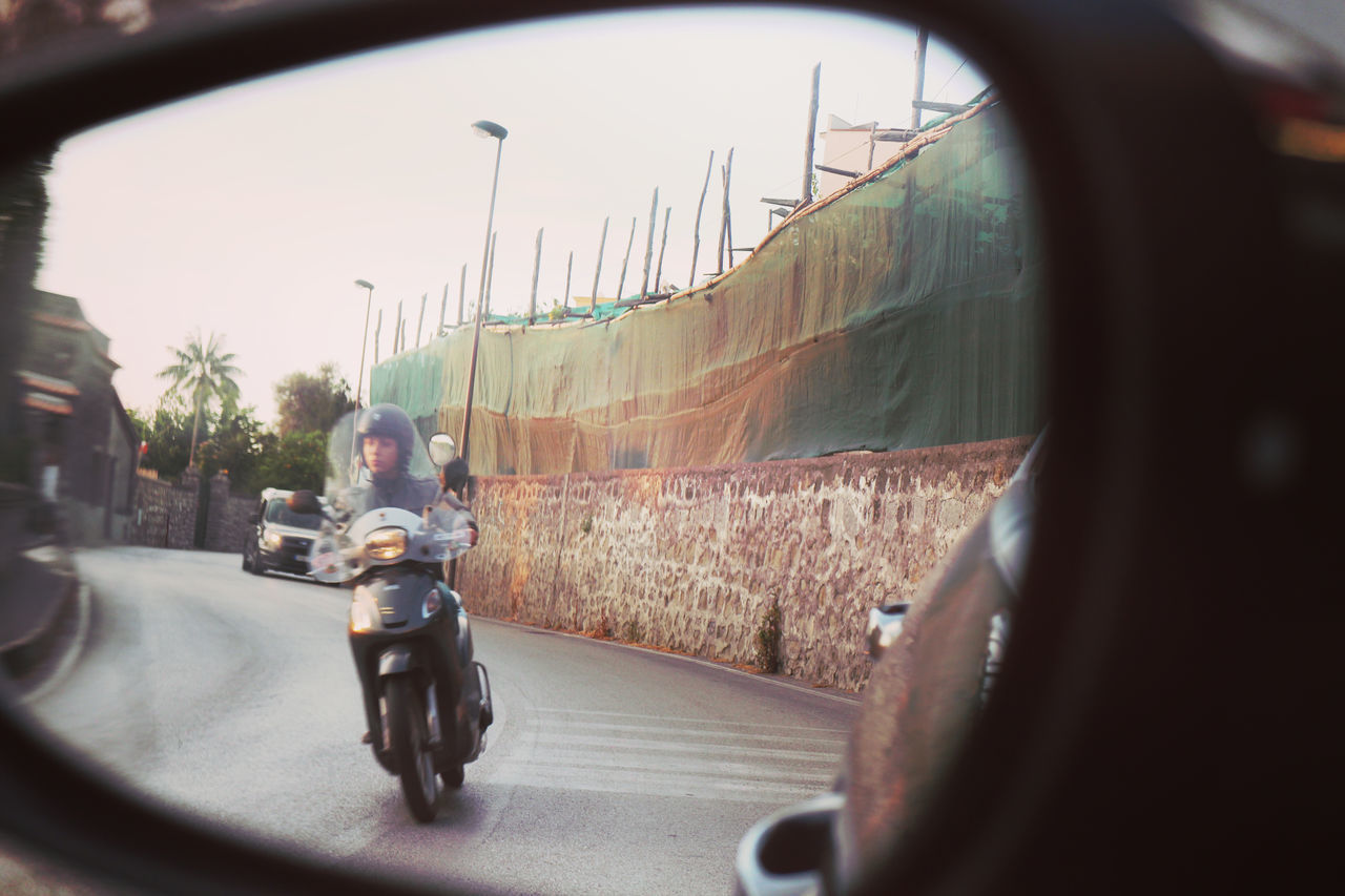 REAR VIEW OF MAN ON SIDE-VIEW MIRROR AT ROAD
