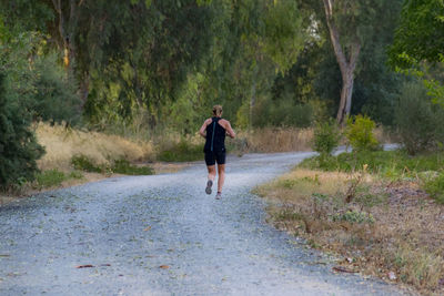 Rear view of man walking on road along trees