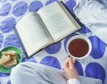 Midsection of woman holding coffee cup while sitting on bed with book
