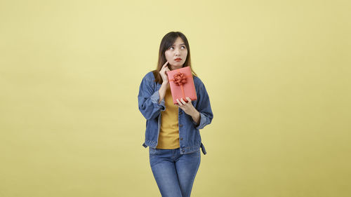 Portrait of young woman standing against yellow background