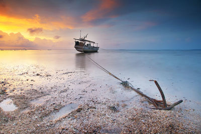 Anchored boat with scenic view of sea against sky during sunset