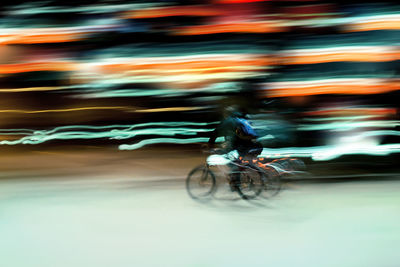 Blurred image of persona riding bicycle against light trail at night
