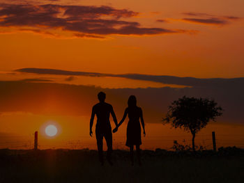 Silhouette men standing on land against sky during sunset