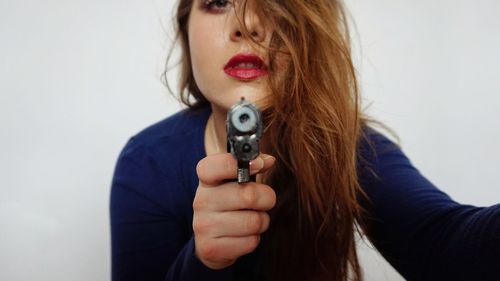Close-up portrait of young woman holding handgun against white background