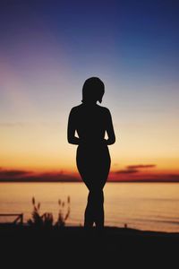 Rear view of silhouette woman standing at beach during sunset