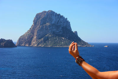 Person on rock by sea against clear sky