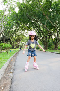 Full length of girl roller skating on road against trees