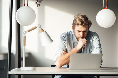 Businessman with hand on chin using laptop at home office