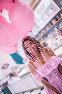 Happy woman holding pink helium balloons while standing in store