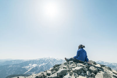 Rear view of man sitting against mountain range against clear sky