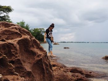 Man standing on rock by sea against sky