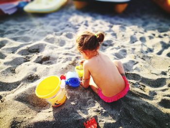 Rear view of shirtless baby girl playing with sand at beach