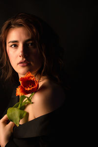 Close-up of young woman holding flower against black background