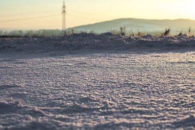 Close-up of snow on shore against sky during sunset