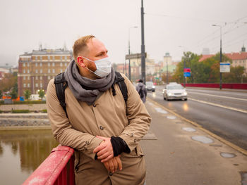 Adult european man wearing a mask, outdoor, stands on a bridge in a city