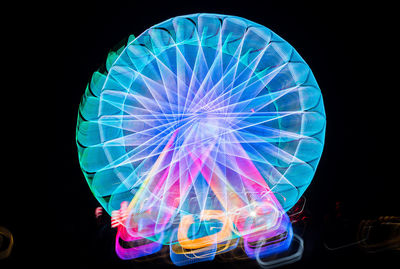 Close-up of illuminated ferris wheel against black background