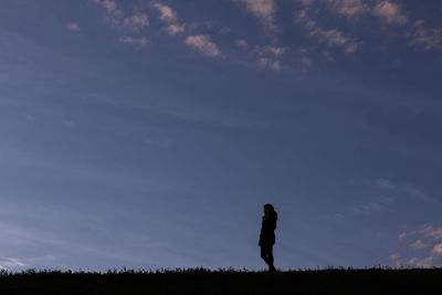 Silhouette person walking on field against sky