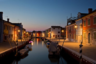 Canal amidst buildings in city against sky at dusk