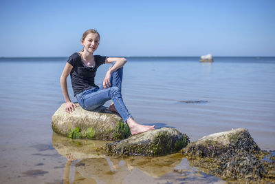 Woman sitting on rock by sea against sky