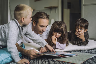 Male child care worker reading story book to students in kindergarten