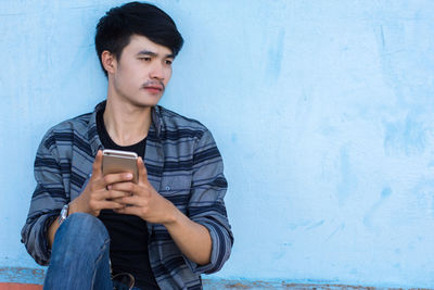 Young man using mobile phone against wall