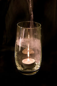 Close-up of pouring water in illuminated tea light candle on table