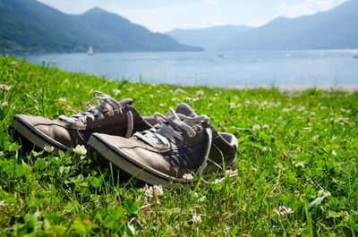 Pair of shoes on grass by river and mountains against sky