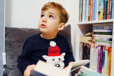 Cute boy looking away while reading book at home