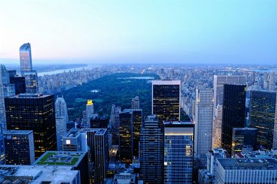 Central park amidst cityscape against clear sky at sunset