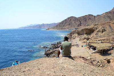 Rear view of man looking at sea while sitting on mountain