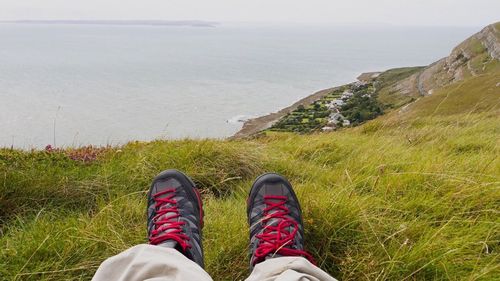 Low section of man on cliff by sea against sky