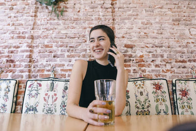 Portrait of a smiling young woman drinking glass against brick wall