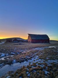 Building on snow covered land against sky during sunset
