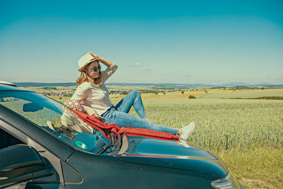 Side view of woman sitting on field against clear sky