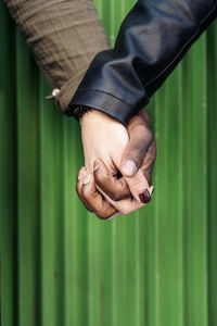 Cropped image of couple holding hands against green corrugated iron