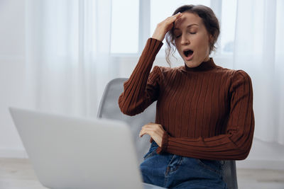 Young woman using laptop while sitting on sofa at home