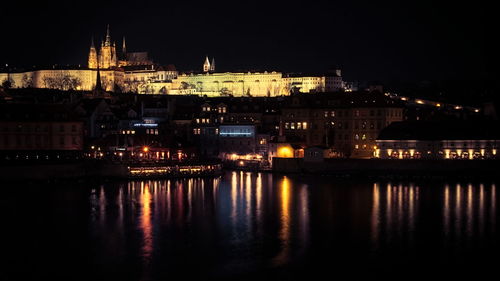 Illuminated city by river against sky at night