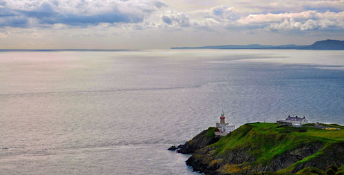 Lighthouse on cliff by sea against sky